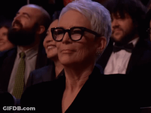 A Woman Wearing Glasses Sits In A Crowd GIF