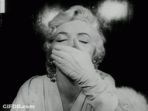 A Woman Wearing Gloves Covers Her Mouth With Her Hand GIF