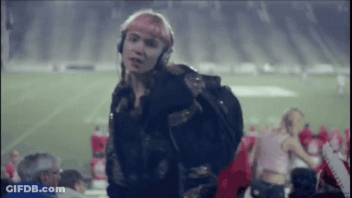 A Woman Wearing Headphones And A Backpack Is Standing On A Football Field GIF
