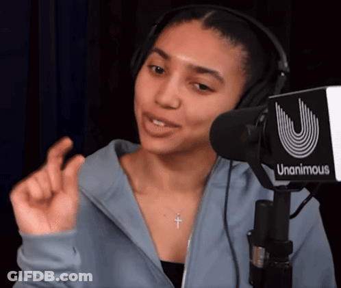 A Woman Wearing Headphones And A Cross Necklace Stands In Front Of A Unanimous Microphone GIF