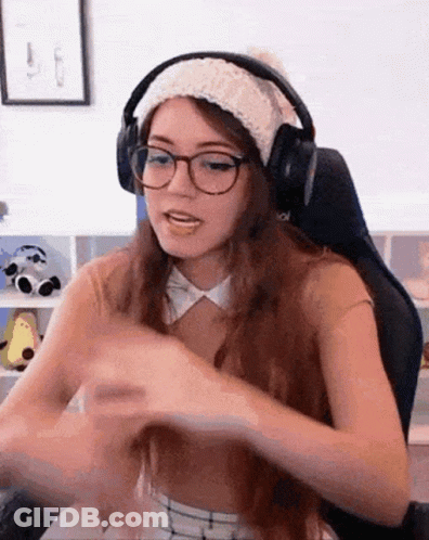 A Woman Wearing Headphones And A Hat Is Sitting In A Chair . GIF