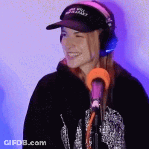 A Woman Wearing Headphones And A Hat Is Standing In Front Of A Microphone . GIF
