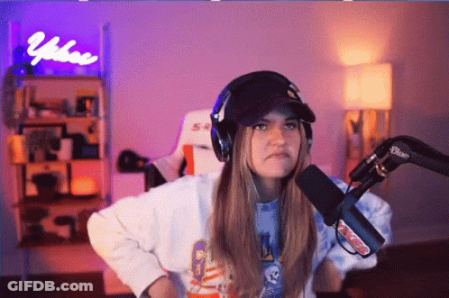 A Woman Wearing Headphones And A Hat Stands In Front Of A Microphone And A Sign That Says Vibe On It GIF