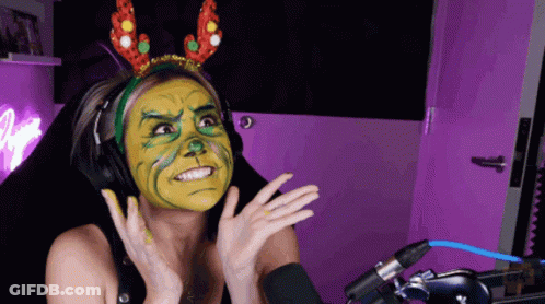 A Woman Wearing Headphones And A Headband With Reindeer Antlers Has A Green And Yellow Face Painted On Her Face GIF