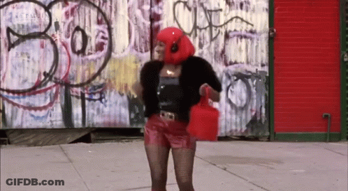 A Woman Wearing Headphones And A Red Head Scarf Stands In Front Of A Graffiti Wall That Says Bo GIF