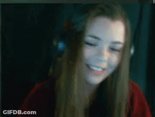 A Woman Wearing Headphones And A Red Shirt Is Smiling While Sitting In Front Of A Computer Screen . GIF