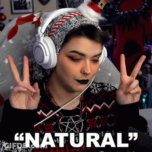 A Woman Wearing Headphones And A Santa Hat Is Giving A Peace Sign With The Words " Natural " Below Her GIF