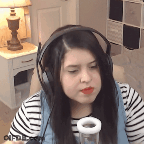 A Woman Wearing Headphones And A Striped Shirt Is Holding A Glass GIF