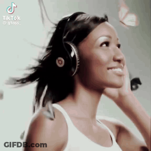 A Woman Wearing Headphones And A White Tank Top Is Smiling . GIF