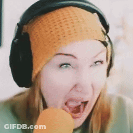 A Woman Wearing Headphones And An Orange Beanie Eating A Carrot GIF