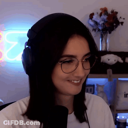 A Woman Wearing Headphones And Glasses Smiles In Front Of A Neon Sign That Says ' E2 ' GIF