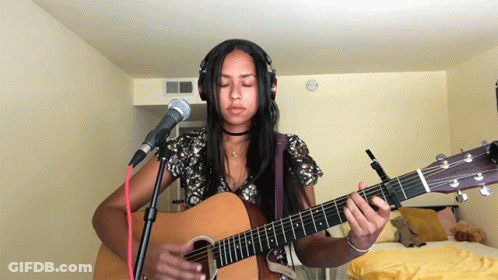 A Woman Wearing Headphones And Playing An Acoustic Guitar GIF