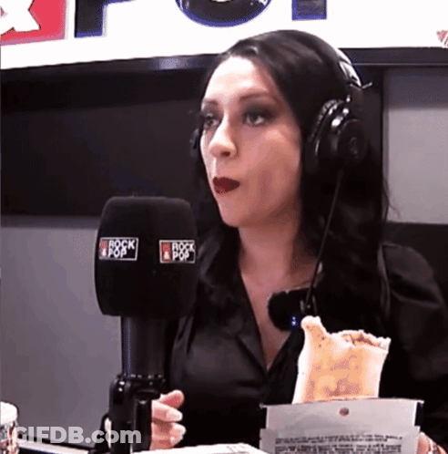 A Woman Wearing Headphones Is Eating A Taco In Front Of A Microphone That Says Rock & Pop GIF