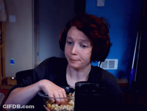 A Woman Wearing Headphones Is Eating Popcorn In Front Of A Blue Wall GIF