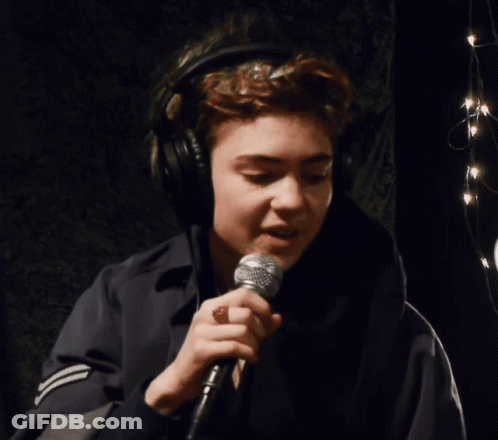 A Woman Wearing Headphones Is Singing Into A Shure Microphone GIF