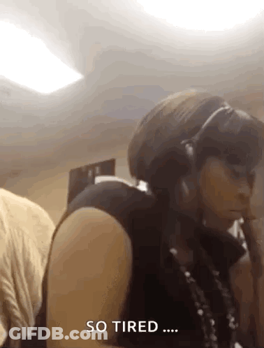 A Woman Wearing Headphones Is Sitting In A Room And Says So Tired . GIF
