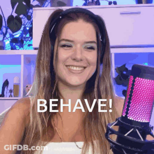 A Woman Wearing Headphones Is Smiling And Holding A Microphone With The Word Behave Written On It GIF