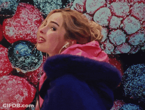 A Woman Wearing Headphones Is Standing In Front Of A Colorful Background Of Berries GIF