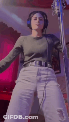 A Woman Wearing Headphones Is Standing In Front Of A Microphone . GIF