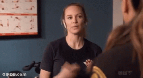 A Woman Wearing Headphones Is Talking To A Man In A Gym While Sitting On An Exercise Bike . GIF