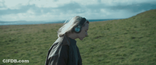 A Woman Wearing Headphones Is Walking Through A Field GIF