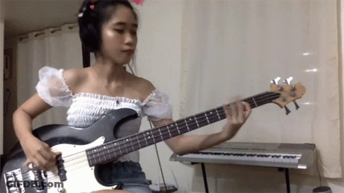 A Woman Wearing Headphones Plays A Bass Guitar GIF