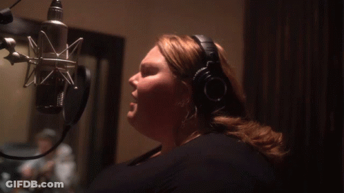 A Woman Wearing Headphones Sings Into A Microphone In A Dark Room GIF