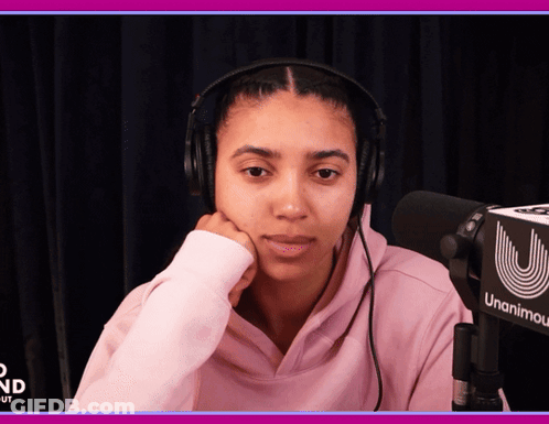 A Woman Wearing Headphones Sits In Front Of A Microphone That Says Unanimity GIF