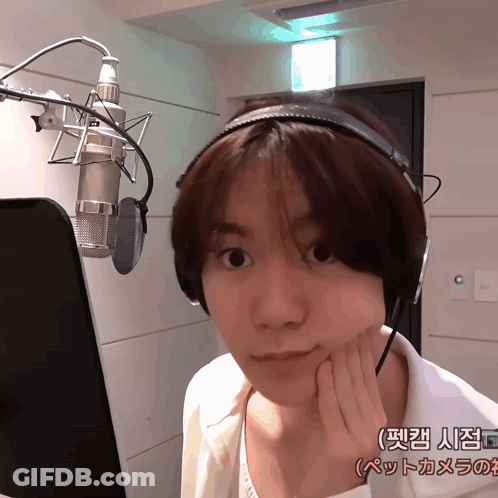 A Woman Wearing Headphones Stands In Front Of A Microphone In A Room With Chinese Writing On The Wall Behind Her GIF