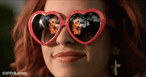 A Woman Wearing Heart Shaped Sunglasses With A Reflection Of Fire GIF