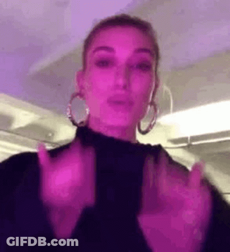 A Woman Wearing Hoop Earrings And A Black Turtleneck Is Making A Funny Face . GIF