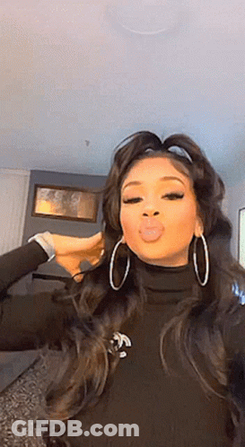 A Woman Wearing Hoop Earrings And A Black Turtleneck Is Making A Funny Face . GIF