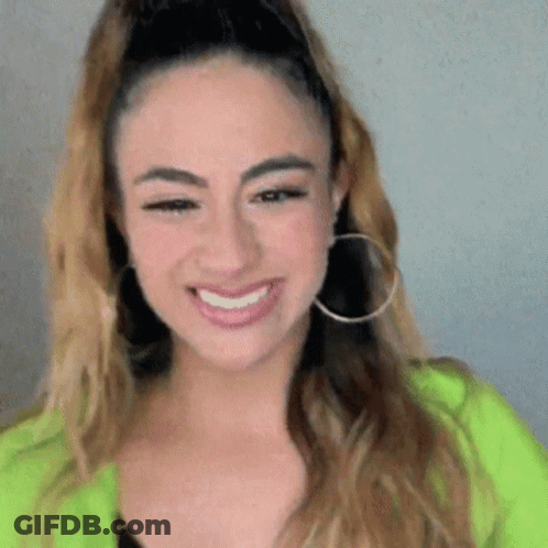 A Woman Wearing Hoop Earrings And A Green Jacket Is Smiling . GIF