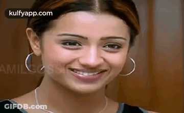 A Woman Wearing Hoop Earrings And A Necklace Is Smiling For The Camera . GIF