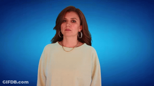 A Woman Wearing Hoop Earrings And A Necklace Looks At The Camera GIF