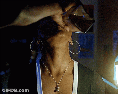 A Woman Wearing Hoop Earrings And A Necklace With A Monkey Pendant Is Drinking From A Glass GIF