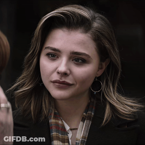 A Woman Wearing Hoop Earrings And A Plaid Scarf Looks At The Camera GIF