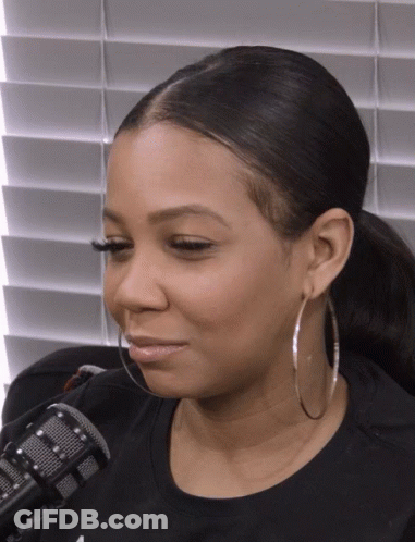 A Woman Wearing Hoop Earrings And A Ponytail Looks At The Camera GIF