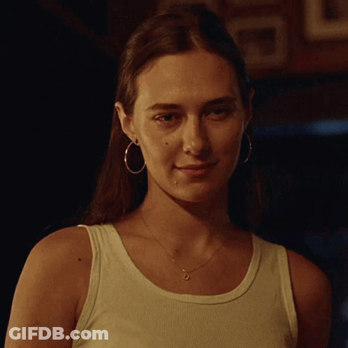 A Woman Wearing Hoop Earrings And A Tank Top Looks At The Camera GIF