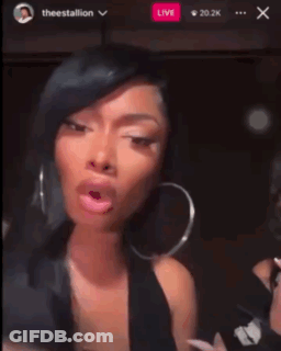 A Woman Wearing Hoop Earrings Is Making A Funny Face In Front Of A Live Audience GIF