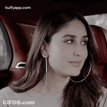 A Woman Wearing Hoop Earrings Is Sitting In A Car And Looking At The Camera . GIF