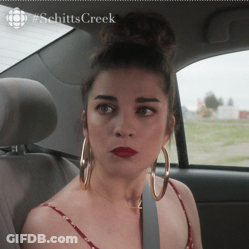 A Woman Wearing Hoop Earrings Is Sitting In The Back Seat Of A Car With #Schitts Creek Written On The Bottom GIF