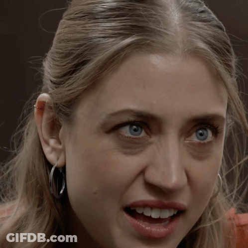 A Woman Wearing Hoop Earrings Is Smiling With Her Mouth Wide Open GIF