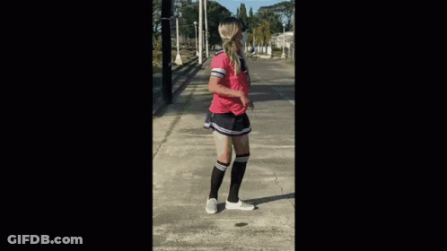 A Woman Wearing Knee High Socks And A Pink Shirt Is Standing On A Sidewalk GIF