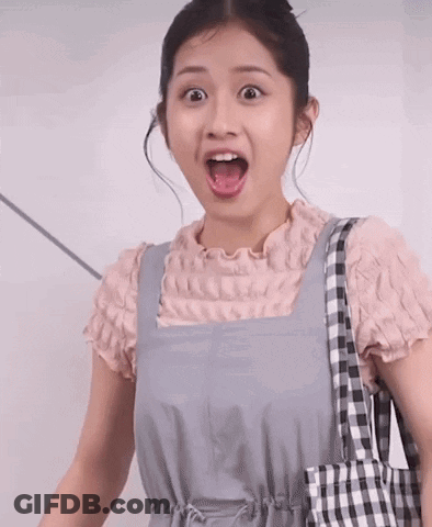 A Woman Wearing Overalls And A Pink Shirt Is Holding A Checkered Bag And Making A Surprised Face GIF