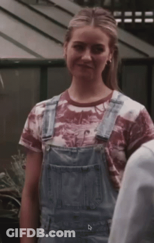 A Woman Wearing Overalls And A T-Shirt With The Letter D On The Bottom Right GIF
