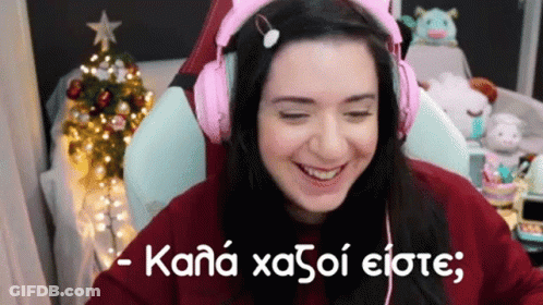 A Woman Wearing Pink Headphones Is Sitting In Front Of A Christmas Tree And Smiling . GIF
