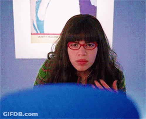 A Woman Wearing Red Glasses Is Sitting In Front Of A Wall With A Picture Of A Woman On It GIF