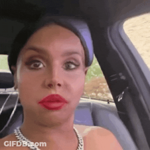 A Woman Wearing Red Lipstick And A Chain Necklace Is Sitting In A Car GIF