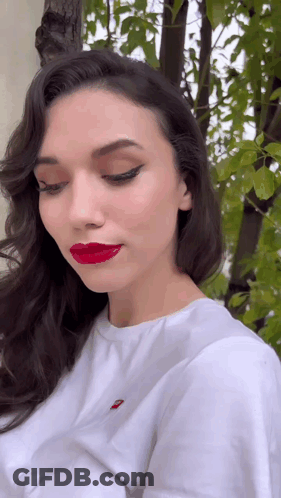 A Woman Wearing Red Lipstick And A White Shirt With A Red Embroidered Levis Logo On It GIF